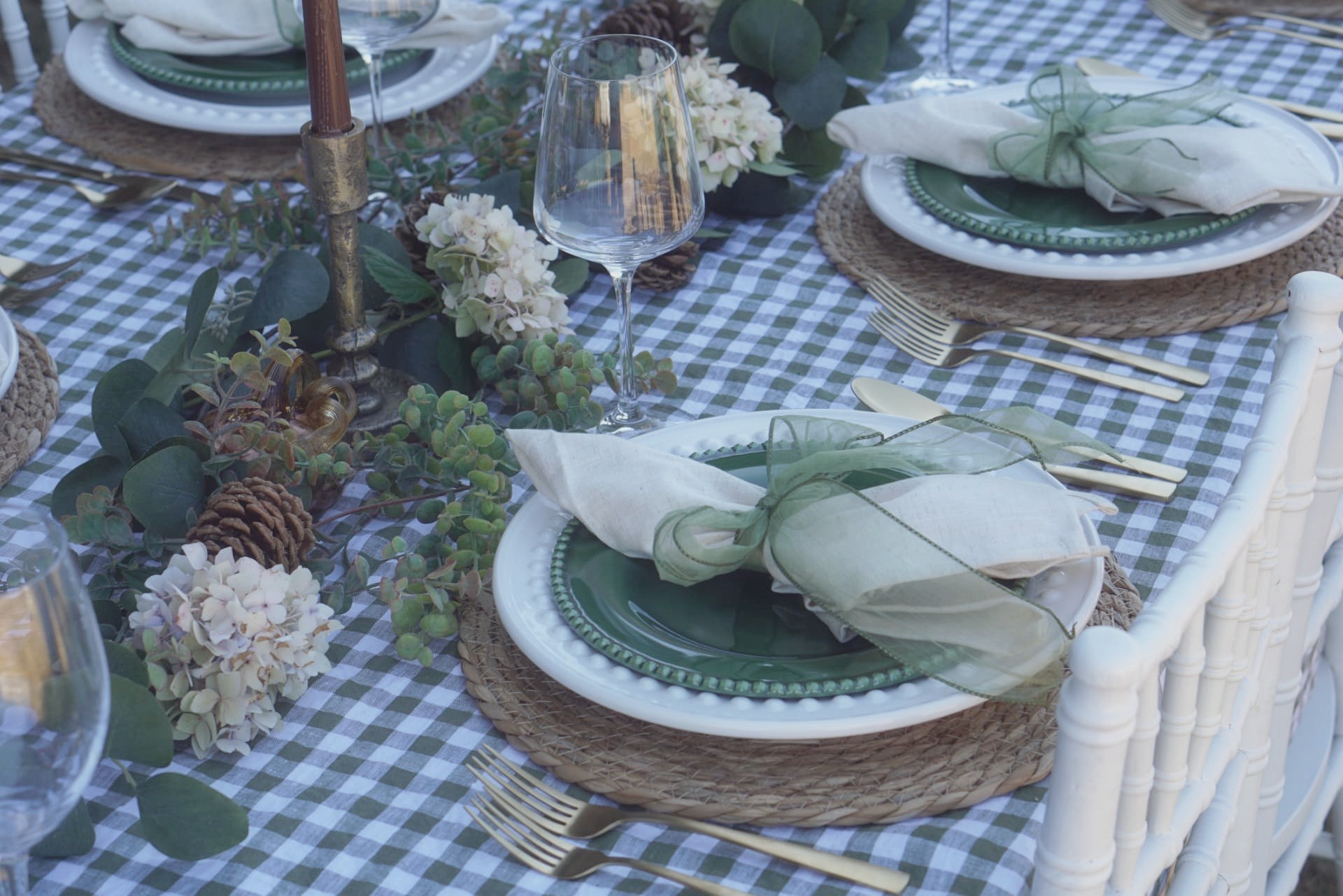 Close-up place setting with a green beaded plate, linen napkin tied with sheer green ribbon, woven charger, and gold flatware
