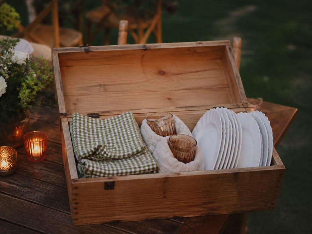 Wooden crate packed with folded gingham linens, glassware, and white plates after an event